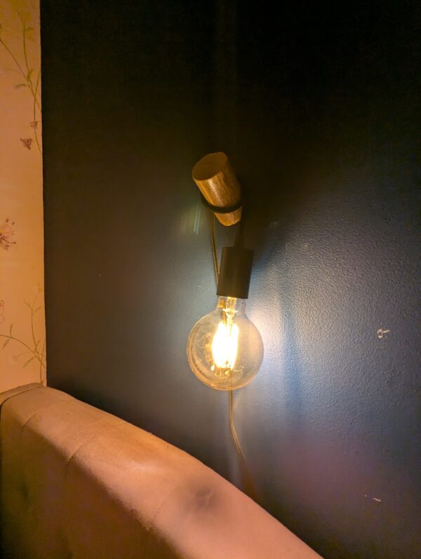 The wooden wall light at night, showing the cosy glow of the light at low brightness